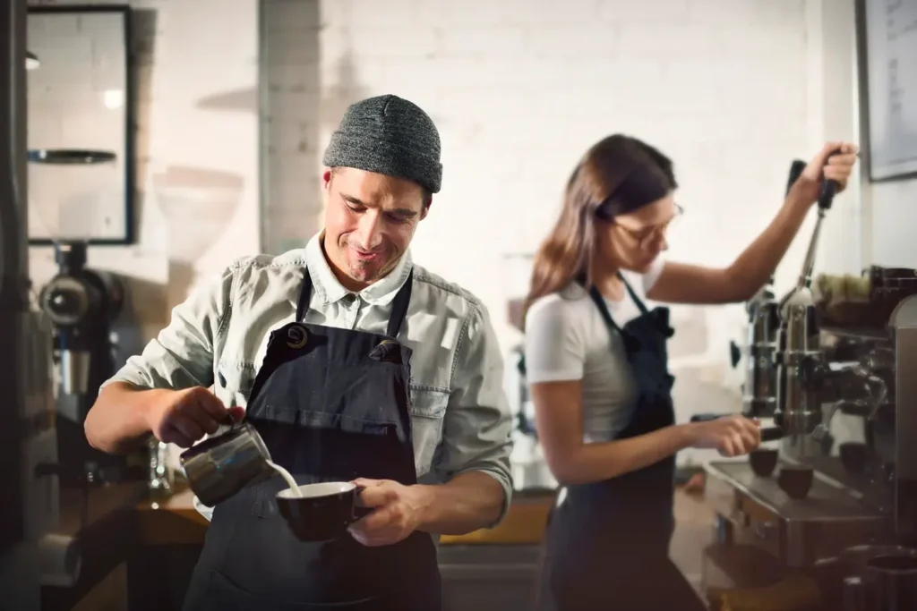 Two baristas working behind a coffee counter preparing drinks for customers